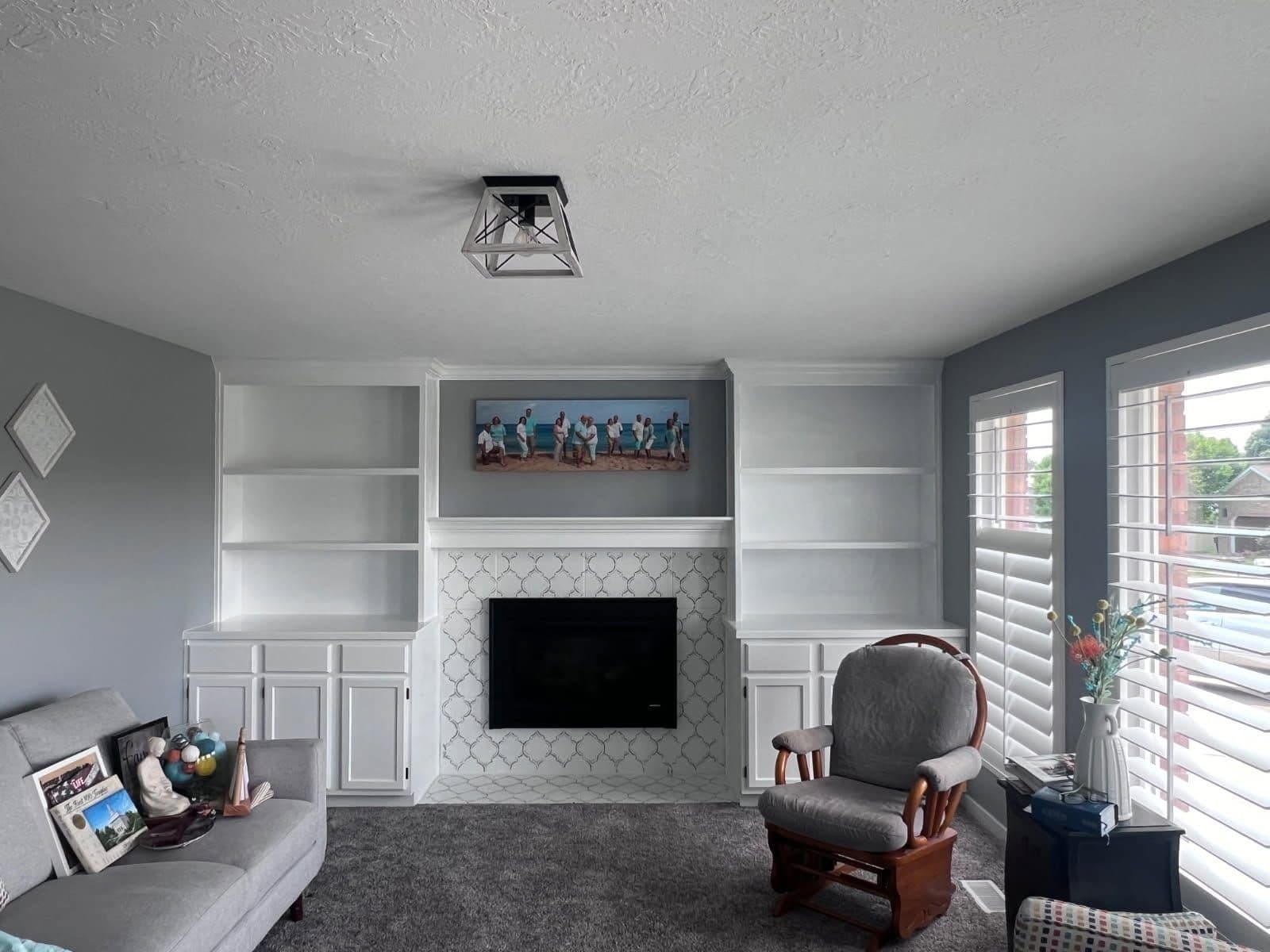 Living room with soft gray walls and crisp white-painted built-in shelving around a tiled fireplace.