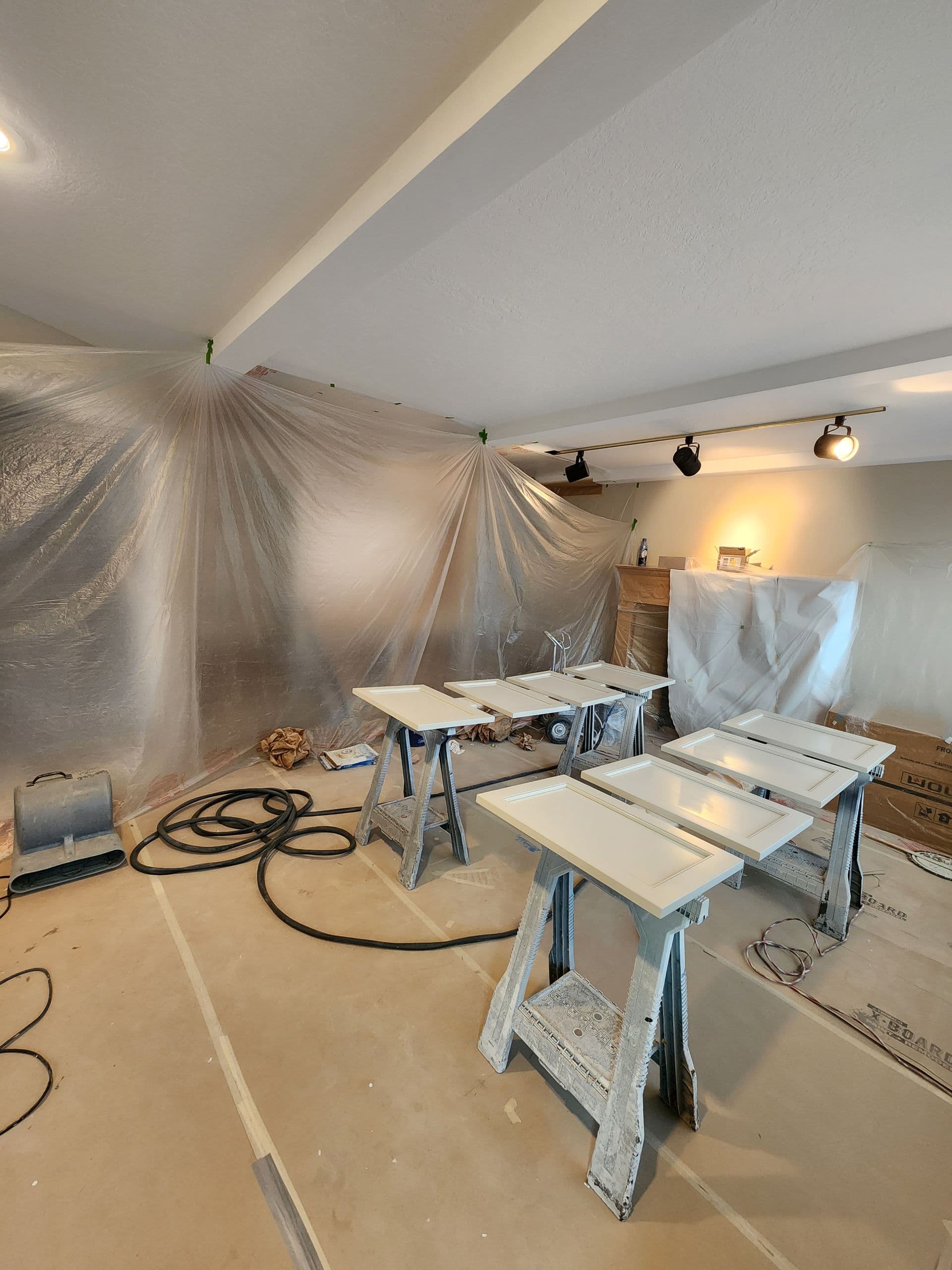 A room fully masked in plastic with cabinet doors drying on sawhorses — professional prep and spray setup.